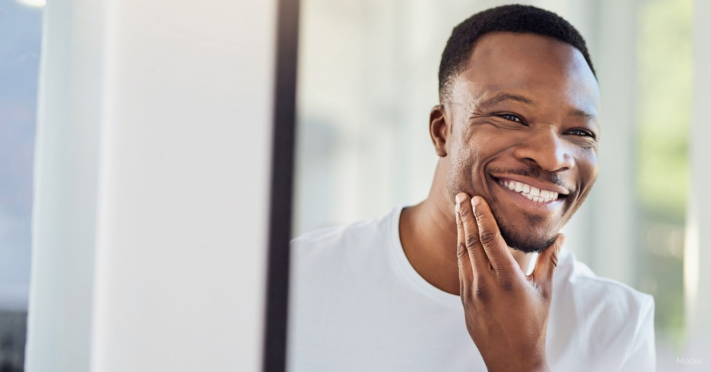 A man examining his face in the bathroom mirror. (Model)