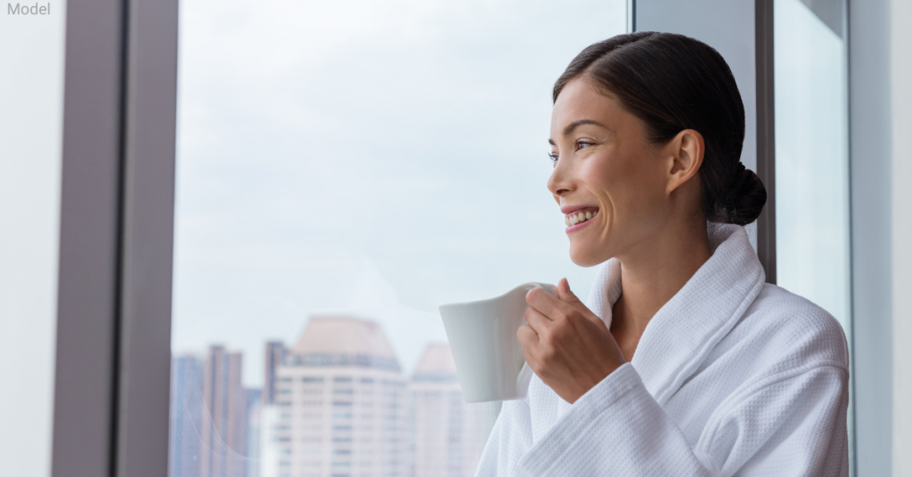 A woman looking out her apartment window while drinking coffee