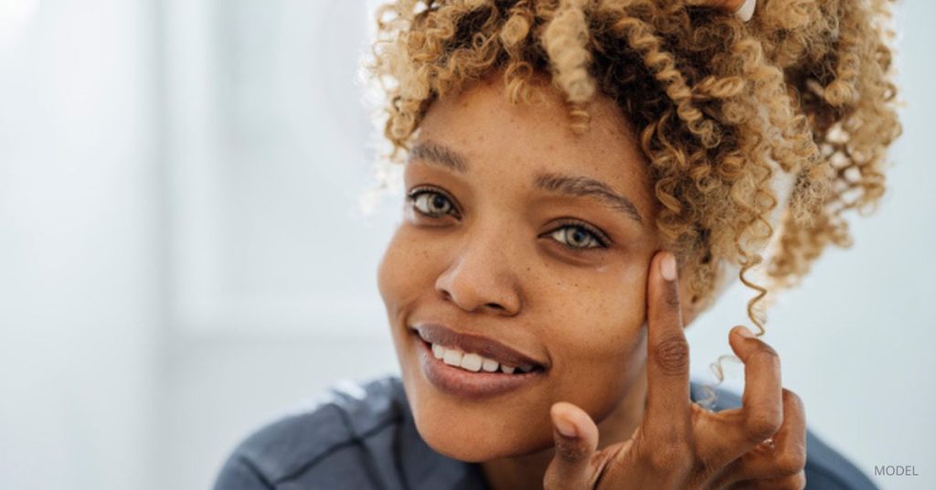 Woman with clear and beautiful skin (model) touches her face while looking at the camera.