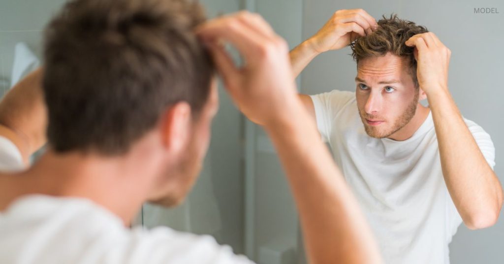 Man (model) examines his hair in the mirror.