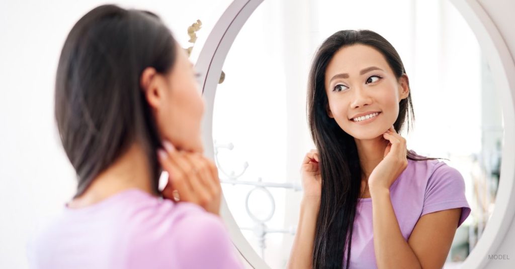 A woman smiling at her reflection in the mirror. (Model)